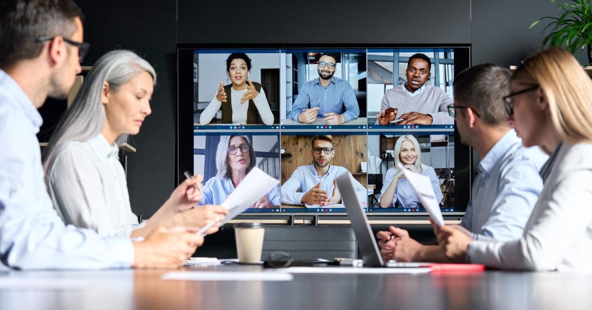 Hybrid work environment - colleagues meeting at table in the office and remote guests on screen